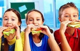 grupo de crianças comendo um sanduíche na escola