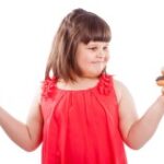 criança obesa escolhendo entre uma maça e um donuts