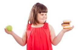 criança obesa escolhendo entre uma maça e um donuts