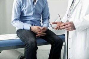 Homem sentado na maca enquanto médico o examina.