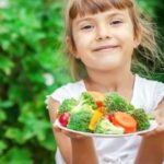 menina sorrindo mostrando um prato com legumes e verduras