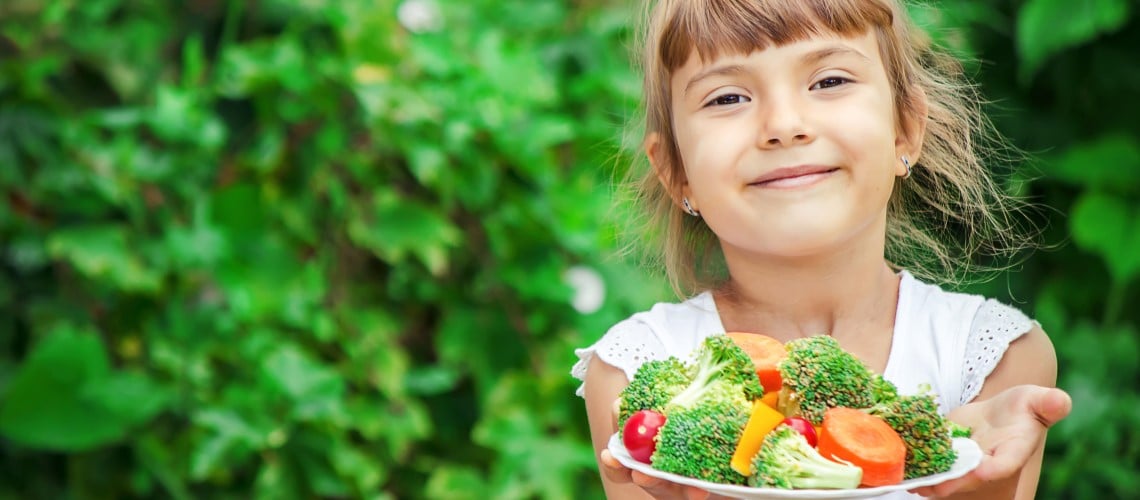 menina sorrindo mostrando um prato com legumes e verduras