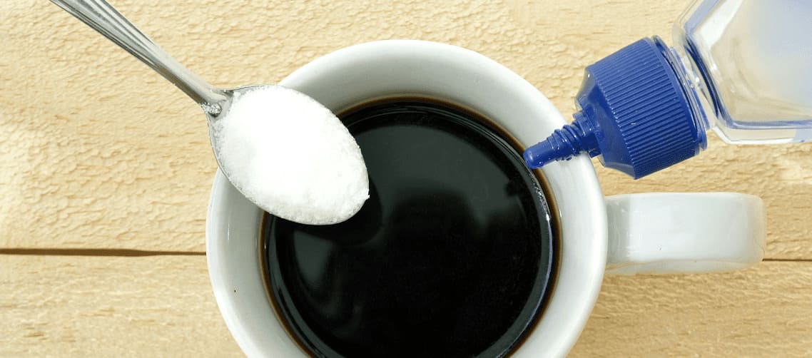 Foto de cima de xícara de café com colher de açúcar e frasco de adoçante.
