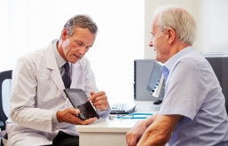 Imagem de um médico mostrando a um senhor um raio X em um tablet