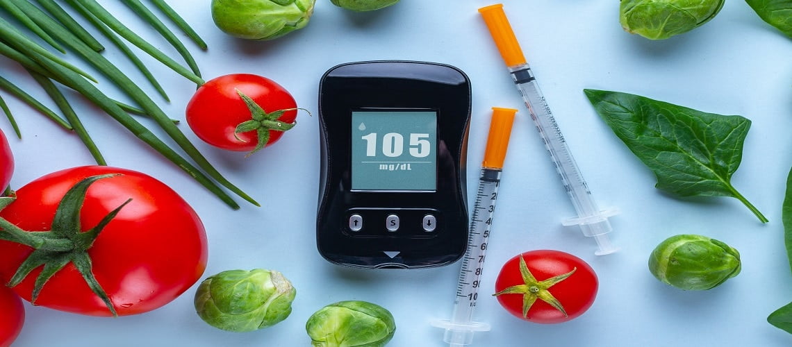 medidor de insulina digital, duas seringas e legumes espalhados na mesa