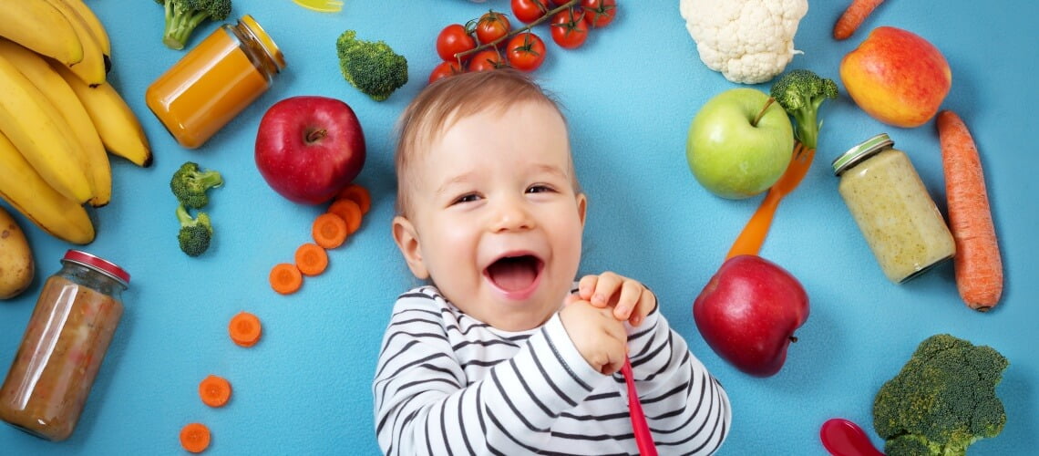 bebê sorrindo com frutas, legumes e potes de vidro em volta