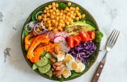 imagem de um prato verde com vários legumes e um garfo do lado.