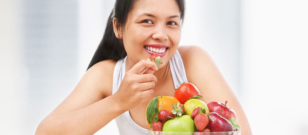 Mulher feliz comendo legumes e frutas saudáveis.