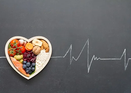 Prato em formato de coração com alimentos saudáveis dentro, em cima de mesa com frequência de batimentos cardíacos desenhada.