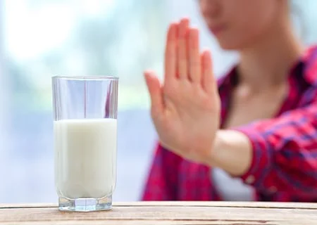 Copo de leite em cima da mesa e, ao fundo, mulher com a mão levantada em sinal de "não"