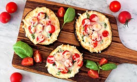 Minipizzas com queijo, tomate e folhas em cima de tábua de madeira