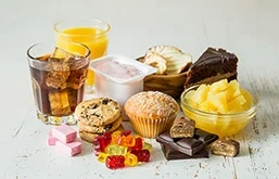 Mesa com diversos alimentos ricos em açúcar, como bolos, pedaços de gelatina, bolachas, chocolates e sucos