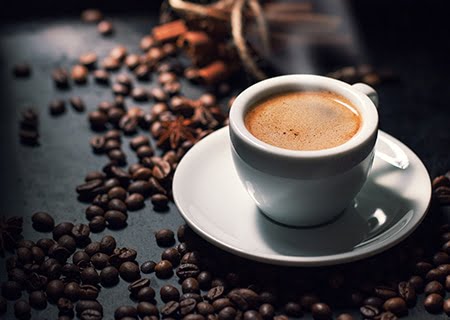 Xícara de café em cima de mesa com grãos de café ao lado