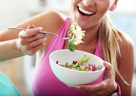 Mulher sorrindo comendo salada em bowl