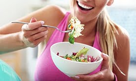 Mulher sorrindo comendo salada em bowl