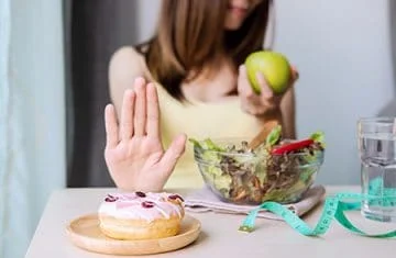 Mulher negando doce e comendo salada e maçã verde