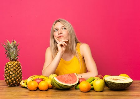 Mulher pensativa sentada em mesa com frutas