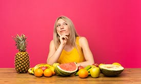 Mulher pensativa sentada em mesa com frutas