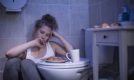 Mulher no banheiro comendo, com cara de preocupada