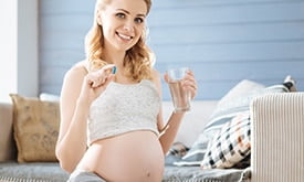 Mulher grávida com vitamina em uma mão e copo de água na outra, sorrindo