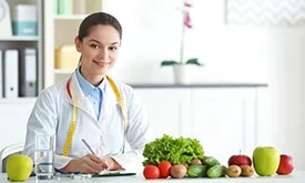 Nutricionista sorrindo atrás de mesa com verduras