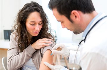Mulher recebendo aplicação de vacina de médico no braço
