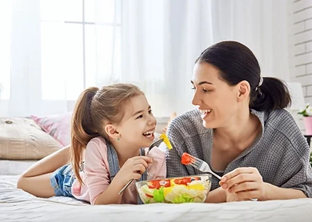 Mãe e filha sorrindo dividindo tigela de salada, com alface e tomates