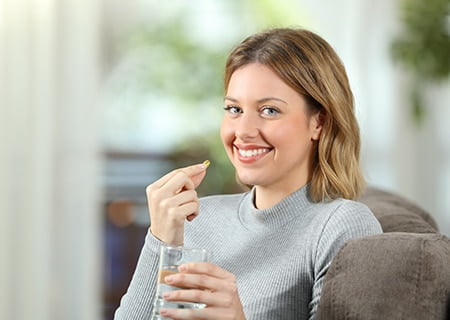 Mulher segurando pílula com uma mão e copo de água na outra