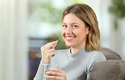 Mulher segurando pílula com uma mão e copo de água na outra