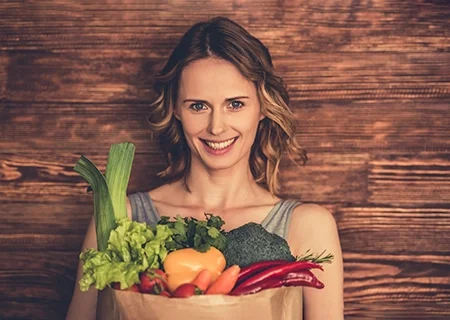 Mulher sorrindo segurando cesta de vegetais