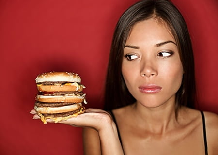 Mulher olhando para sanduíche com expressão de dúvida, se come ou não
