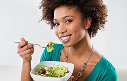 Mulher sorri segurando uma tigela de salada