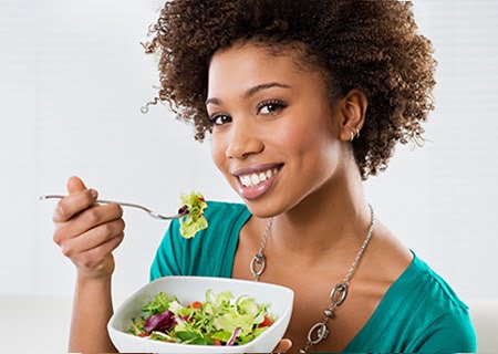 Mulher sorri segurando uma tigela de salada