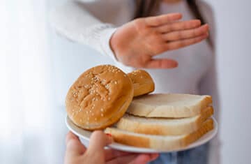 Uma pessoa oferecendo pães e outra negando. Muita gente acha que cortar glúten da dieta ajuda a emagrecer.