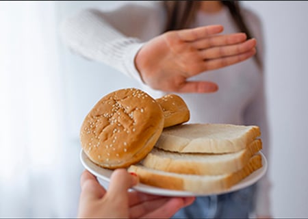 Uma pessoa oferecendo pães e outra negando. Muita gente acha que cortar glúten da dieta ajuda a emagrecer.