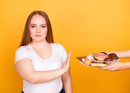 Mulher negando com a mão pessoa que a oferece donuts e bolinhos