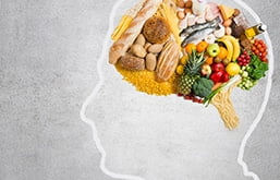 Desenho de cabeça com alimentos no lugar do cérebro, entre frutas, legumes e vegetais