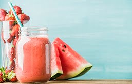 Mesa com suco de melancia em pote de vidro e fatias de melancia. A fruta é um dos alimentos que hidratam o corpo