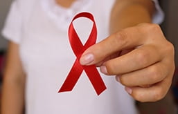 Uma mulher segurando uma fita vermelha, representando o dezembro vermelho. A relação entre alimentação e HIV pode garantir melhores condições de saúde para as pessoas infectadas com o vírus