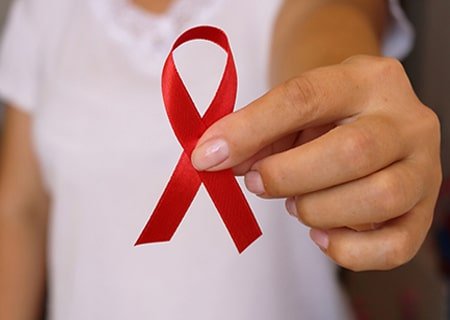 Uma mulher segurando uma fita vermelha, representando o dezembro vermelho. A relação entre alimentação e HIV pode garantir melhores condições de saúde para as pessoas infectadas com o vírus