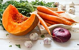 Mesa com cenouras, melão, alho e cebolas - exemplos de alimentos antioxidantes que atuam na prevenção do câncer de pele
