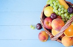 Mesa com diversas frutas em tigela, como uvas, maçãs e pêssegos