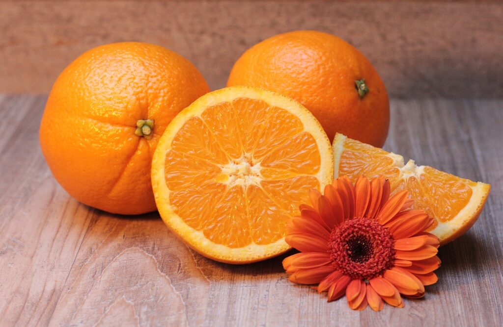 Laranjas inteiras e fatiadas, com uma flor laranja ao lado