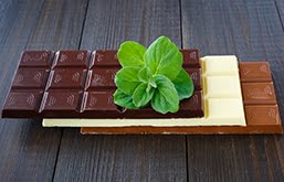 Mesa com tabletes de chocolate ao leite, branco e amargo. Em cima deles, folhas de hortelã.