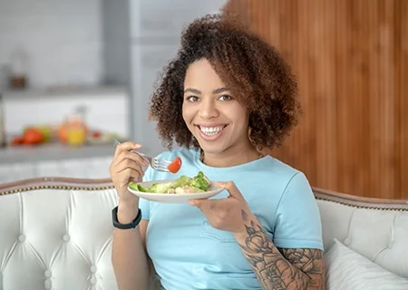 Mulher com tatuagem comendo prato de salada