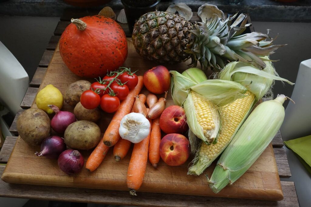 Mesa com vegetais como milho, cenoura, tomates e abacaxi