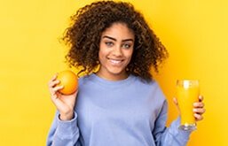 Mulher segurando uma laranja em uma mão e um copo de suco em outra