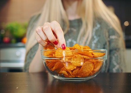 Mulher pegando uma batata chips em pote cheio delas