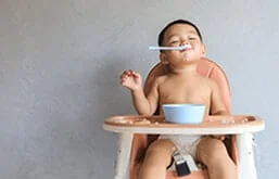 Bebê sentado em cadeira com colher na boca