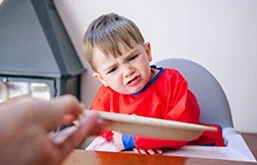 Criança olhando para prato com expressão de rejeição